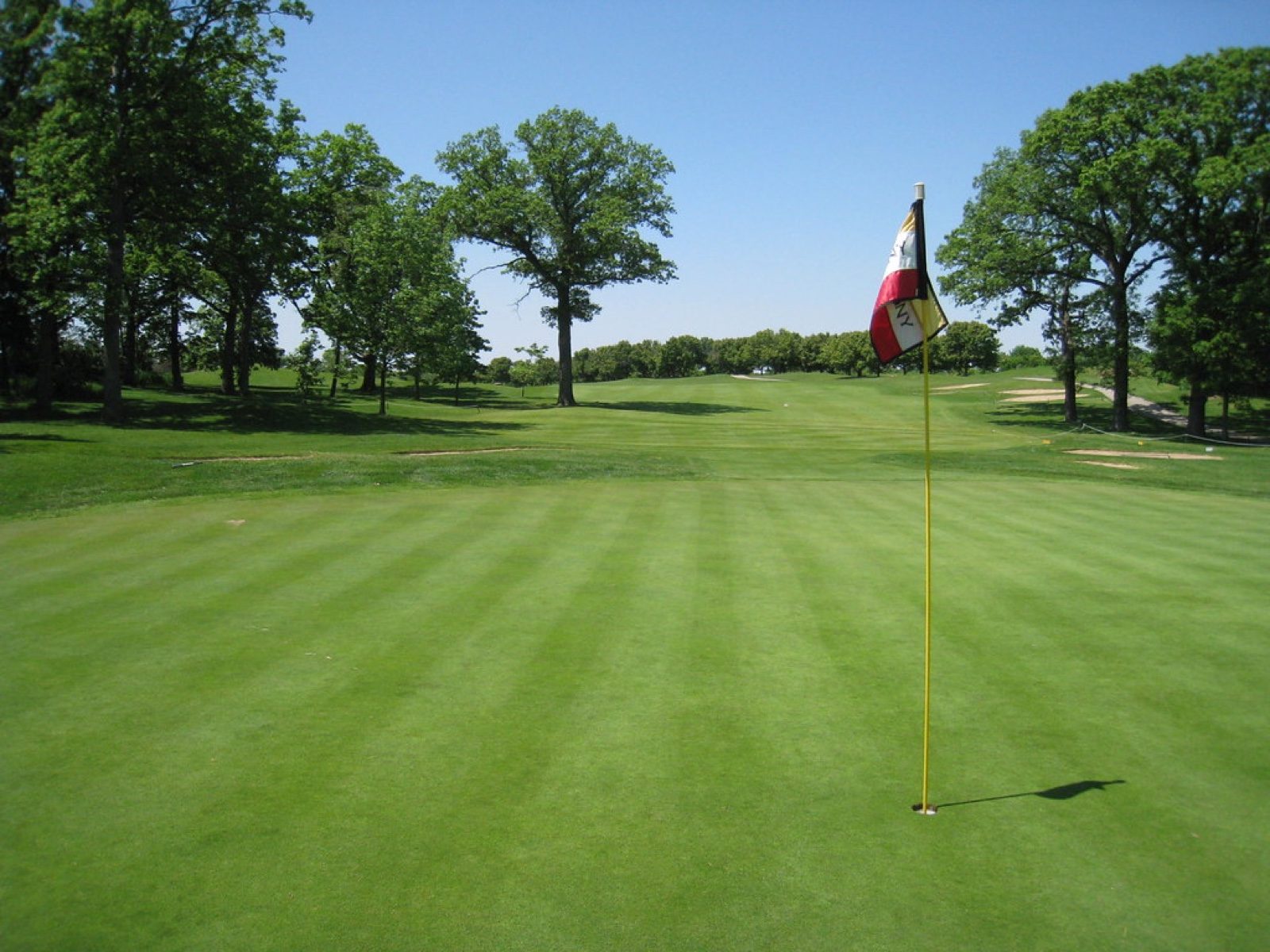 Lush striped golf fairway with the pin flag under a clear blue sky